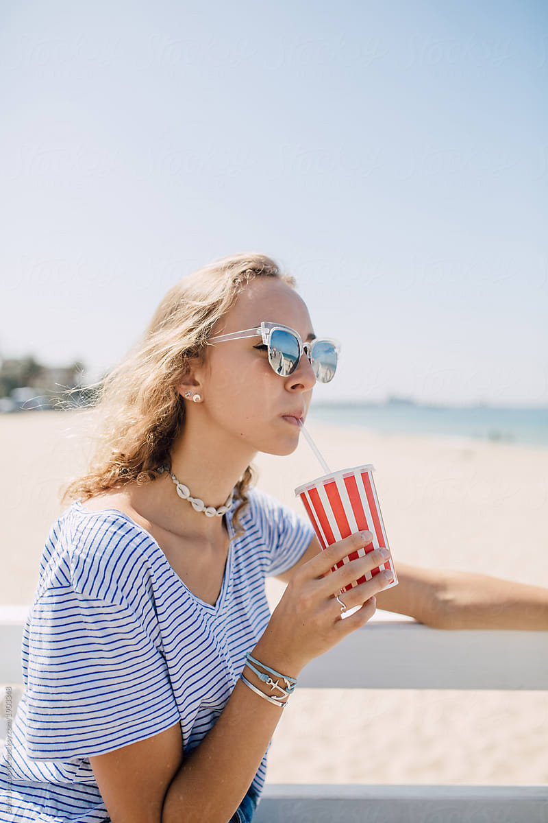 Portrait of beautiful blonde woman drinking juice on the beach