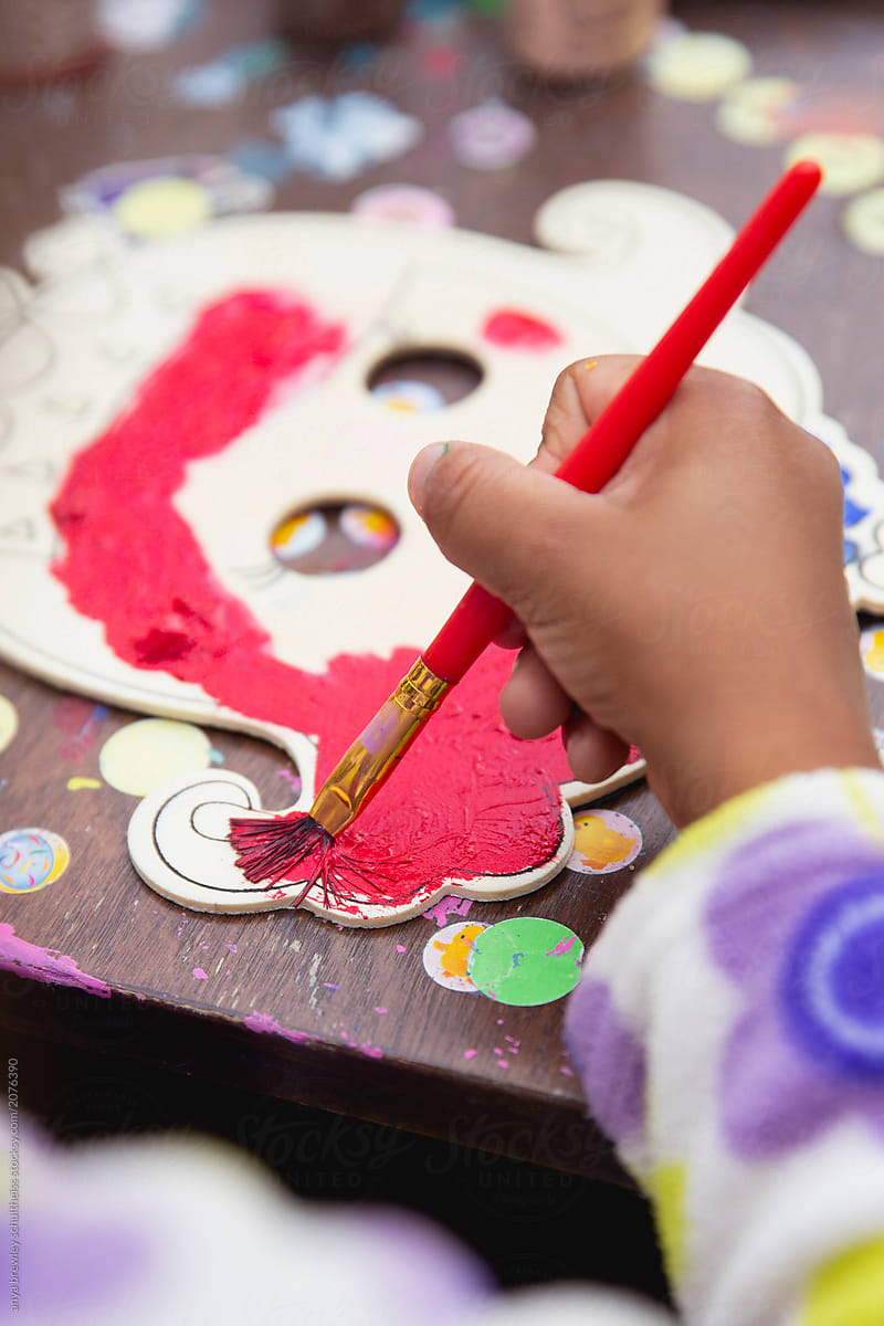 A child painting bright colours onto a wooden mask