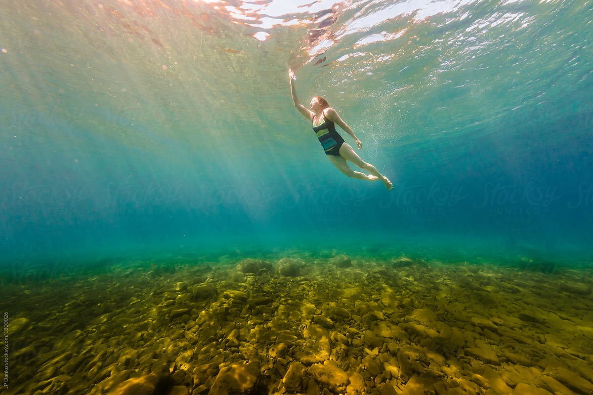 Young Woman Swimming Underwater In Crystal Clear Summer Lake By
