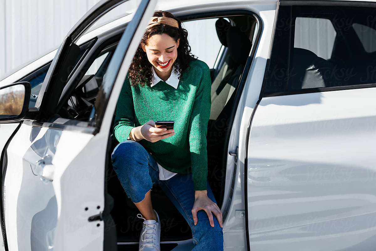 Cheerful female driver browsing smartphone in vehicle
