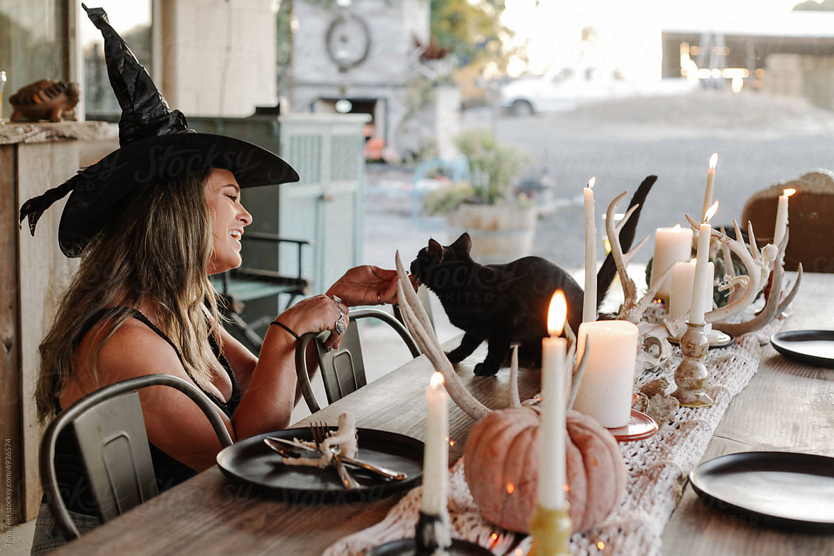 woman wearing witch hat gives black kitten attention