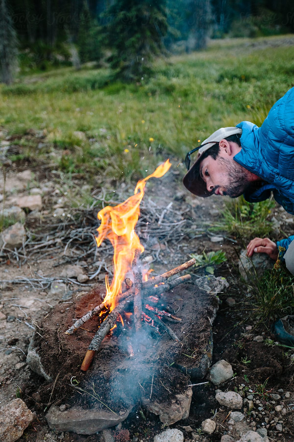 Man Feeding Sticks To Small Fire Outdoors While Camping by Stocksy  Contributor Matthew Spaulding - Stocksy