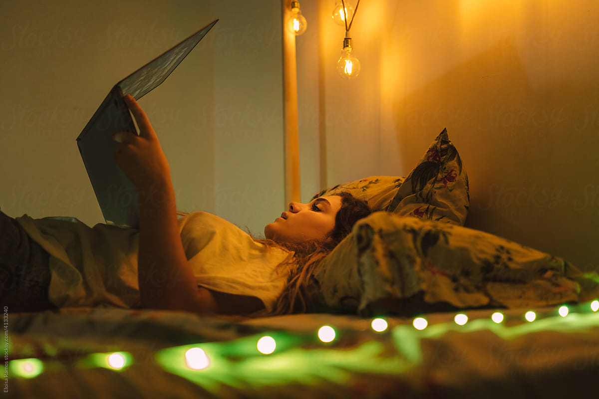 Female with laptop lying on the bed at night