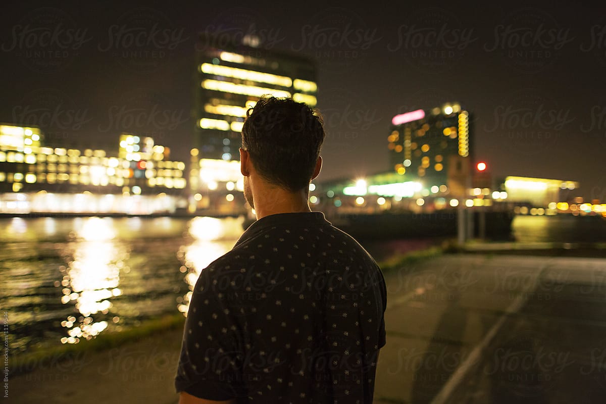 Man overlooking waterfront at night, with city lights in the background.