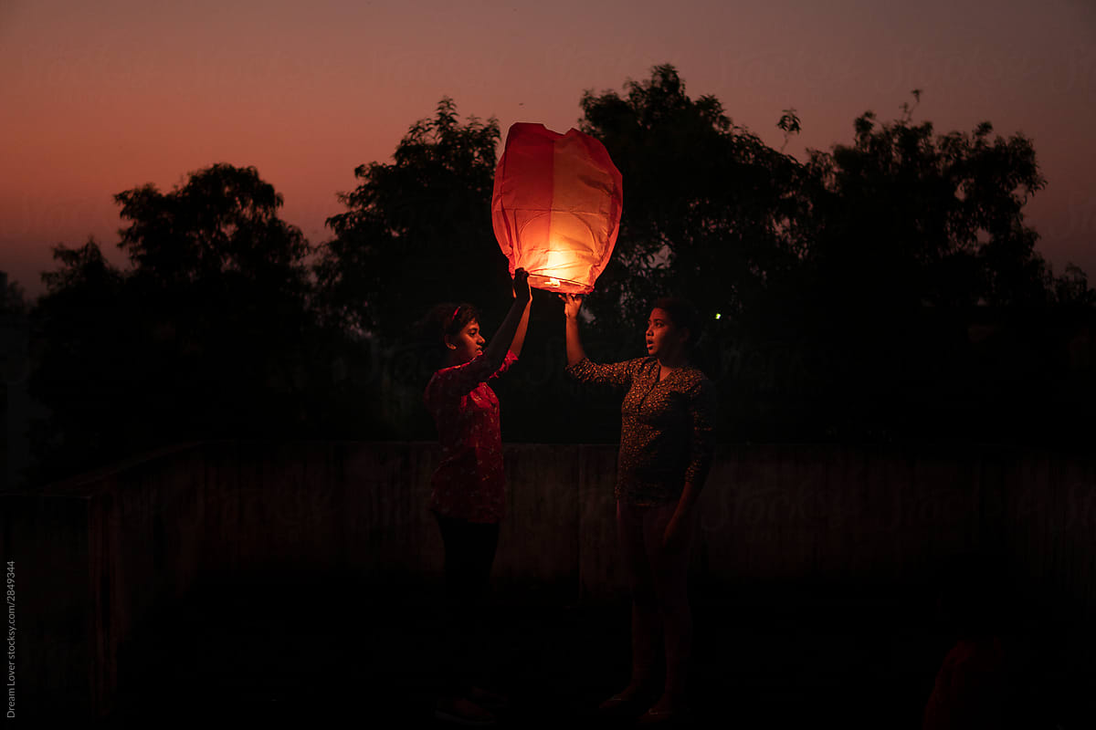 Sisters holding and releasing Chinese lantern at outdoors in the evening time