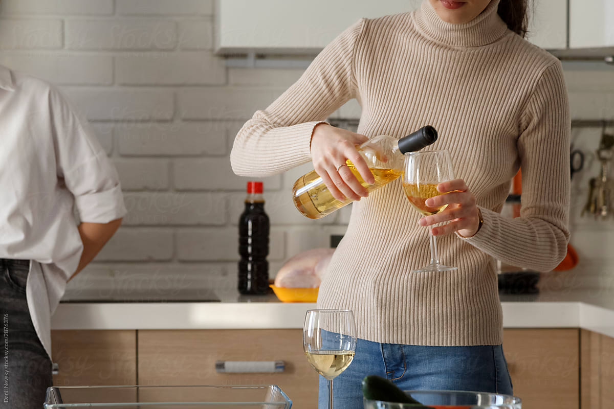 Woman in turtleneck pouring wine to glass in kitchen