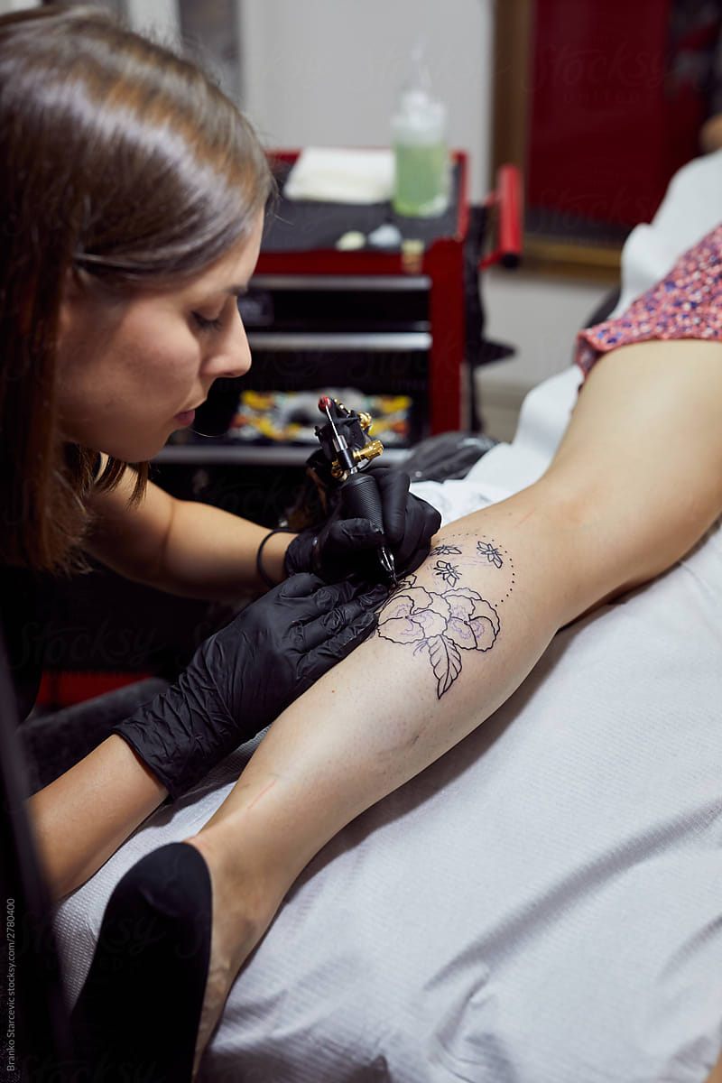 Female tattoo artist doing a tattoo session.