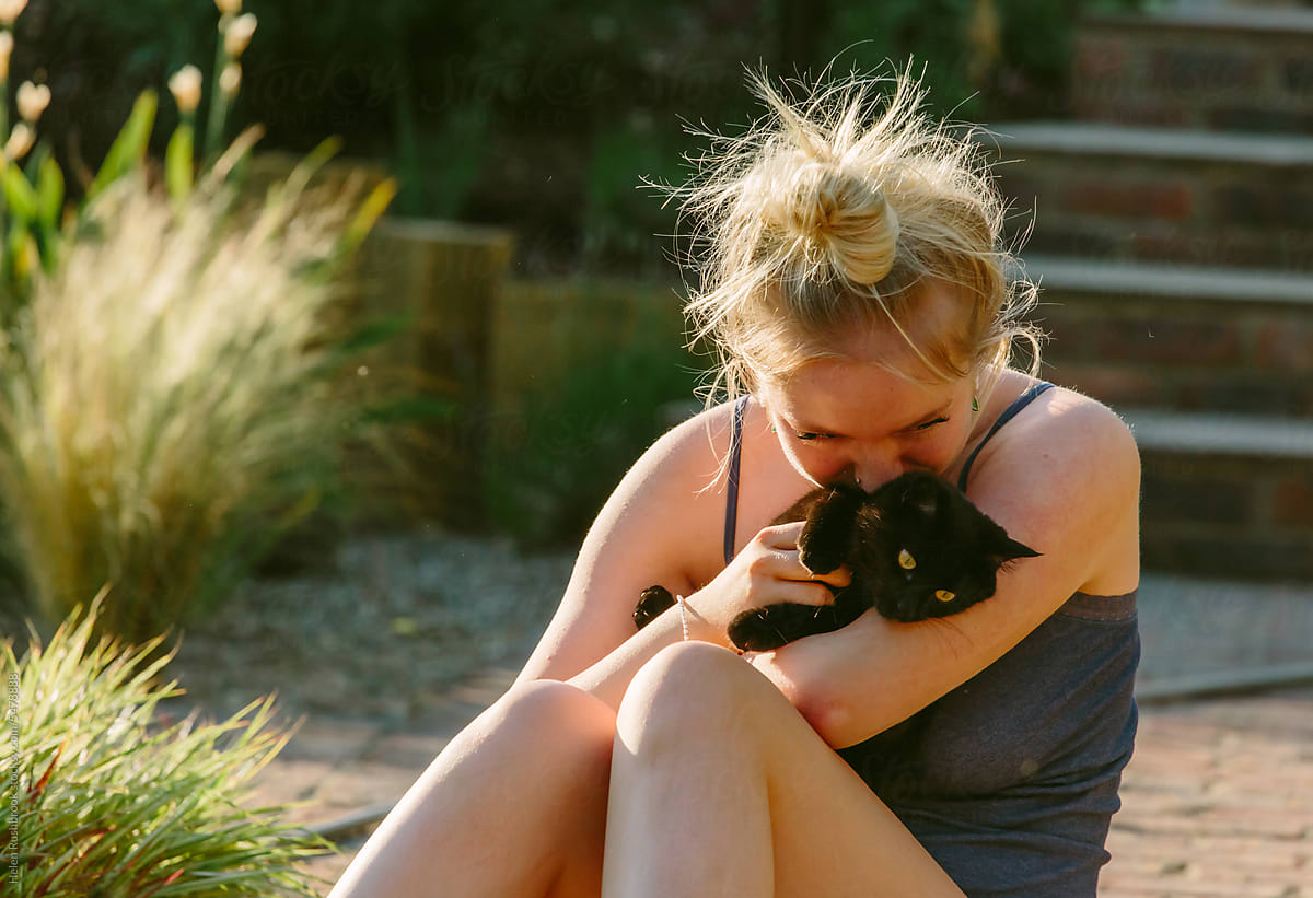 Teenage girl outdoors in summer cuddling her small black kitten