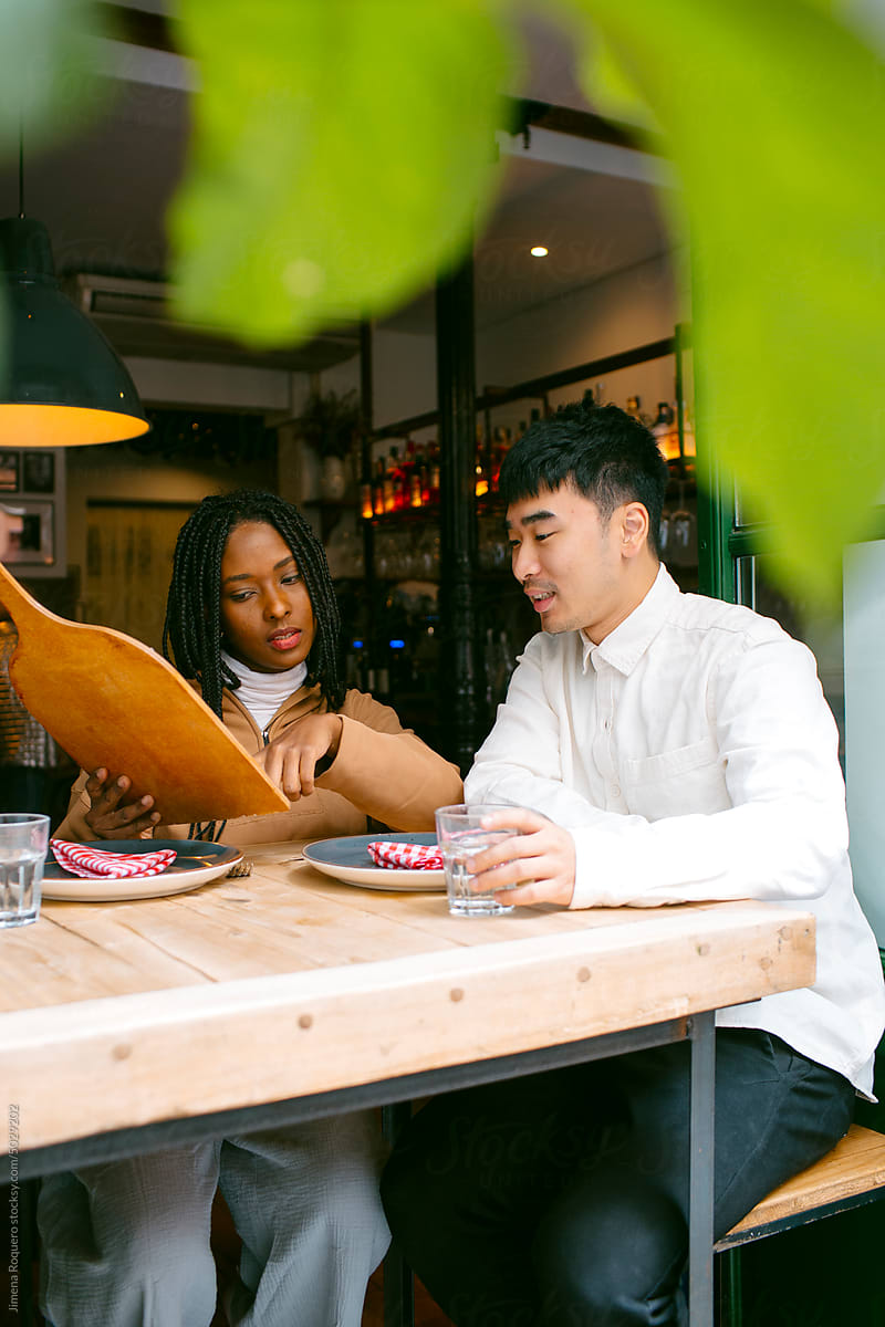 Couple looking at restaurant menu sitting in table by window