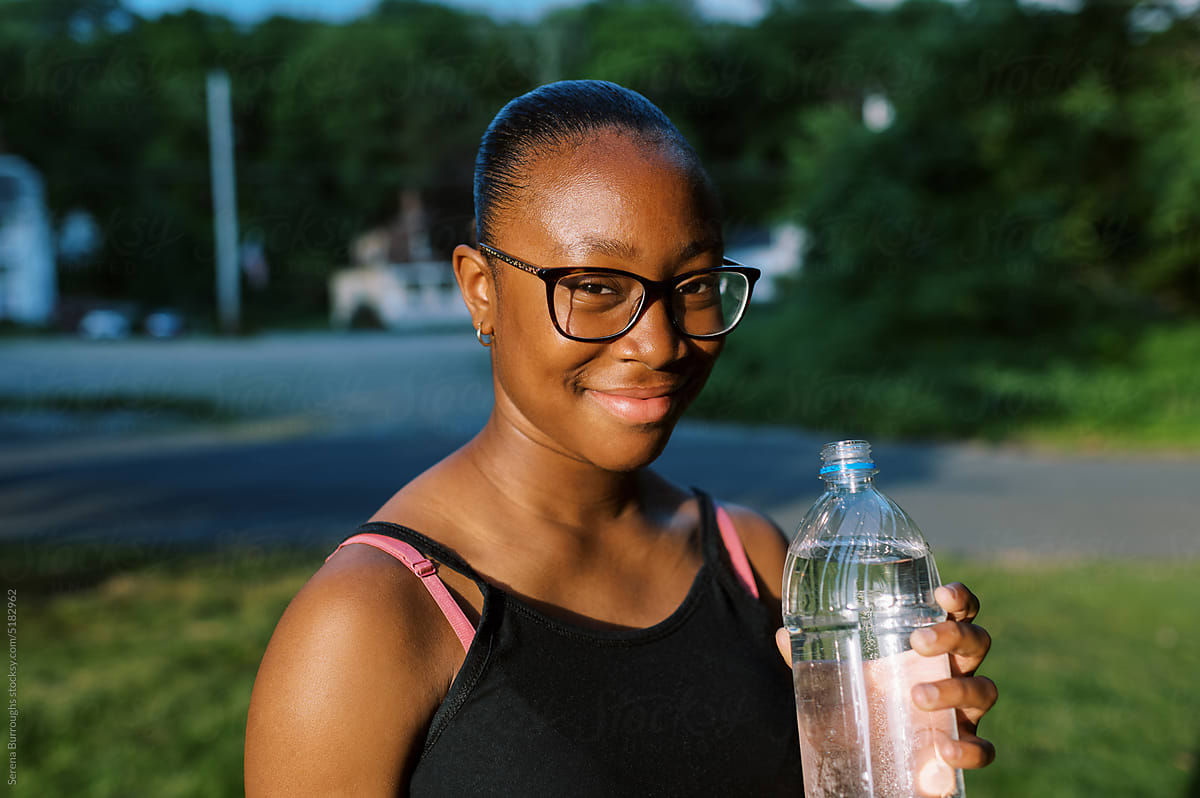 smiling fit black tween girl standing outdoors drinking water
