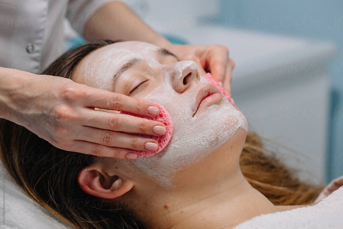 Unrecognizable cosmetician rubbing client face with sponges