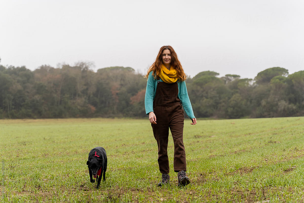 Happy Woman and her dog walking on empty field