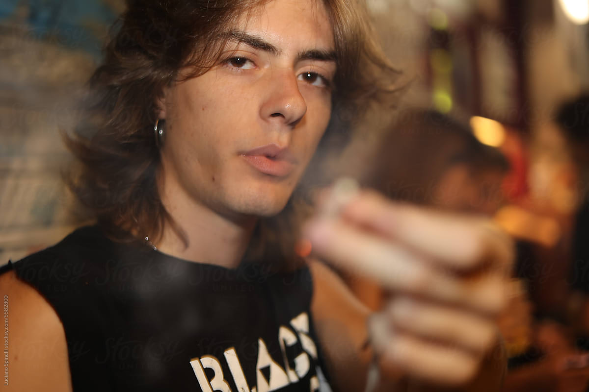 Long hair rock style man smoking and offering cigarette to the camera