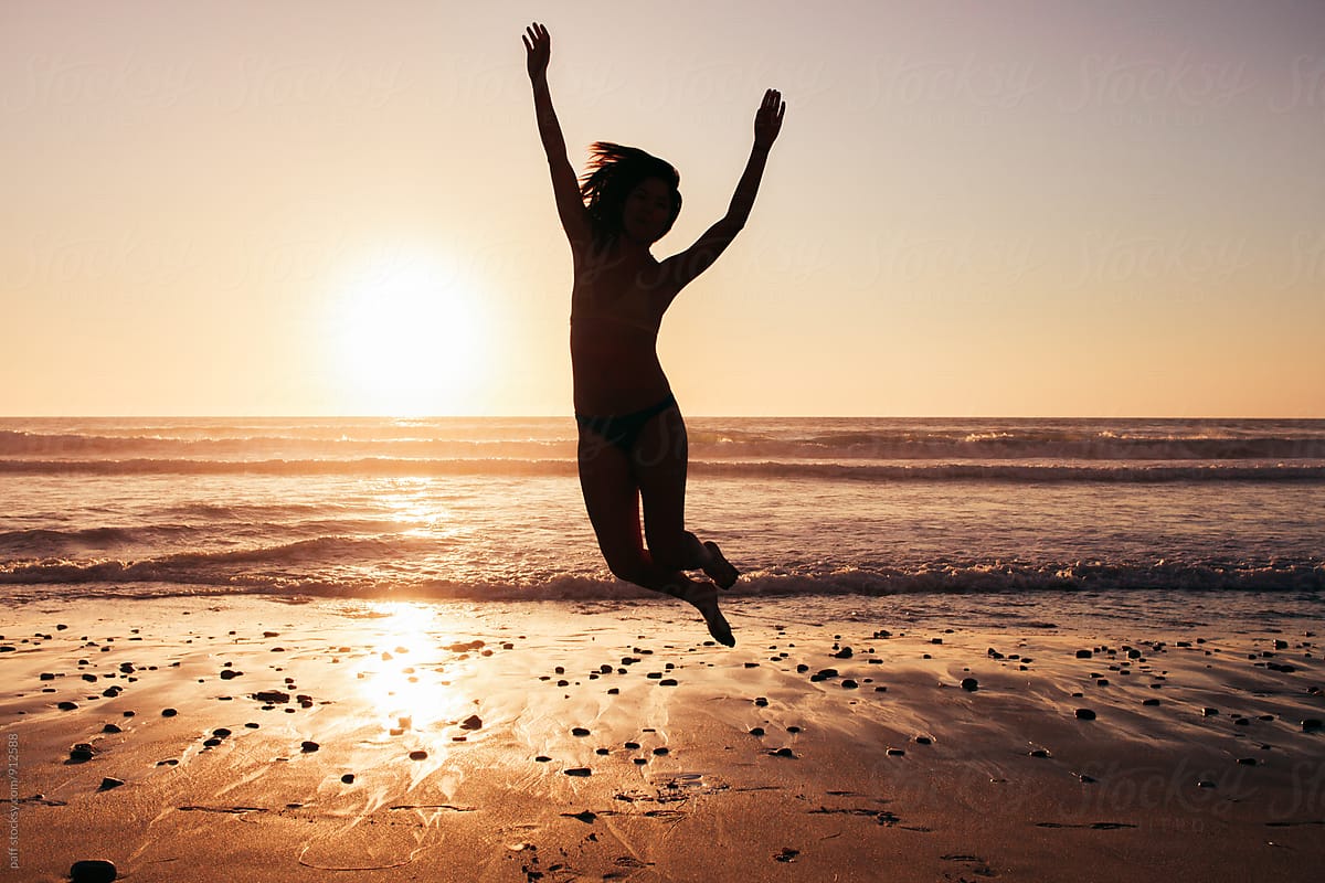 Silhouette of a young woman jumping for joy on the beach in front of the ocean