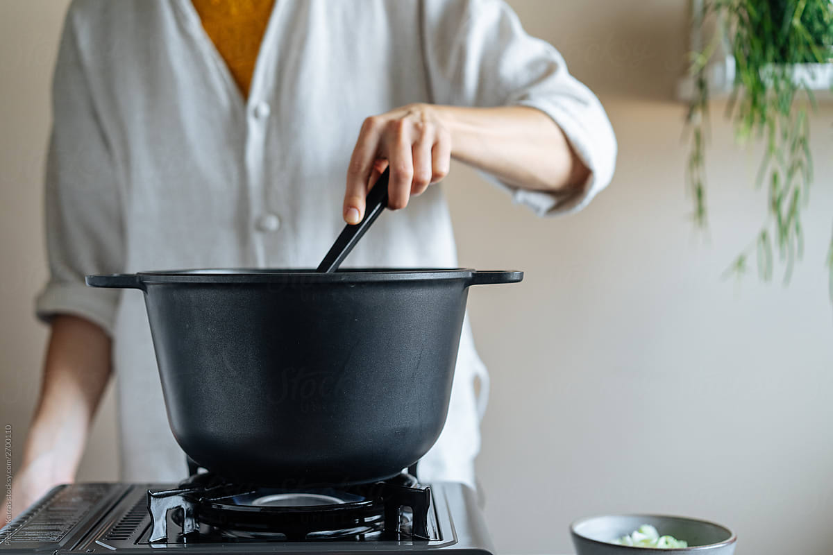 Faceless chef stirring food in black cooking pot on stove