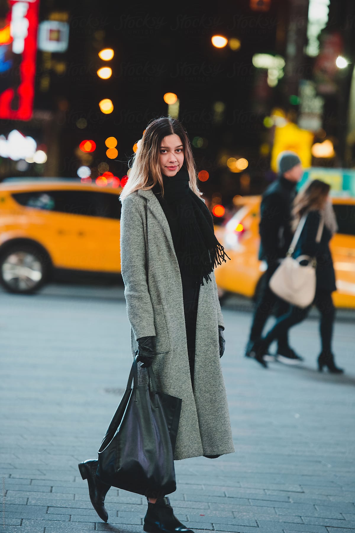 Young Woman Walking Down City Street At Night by Stocksy