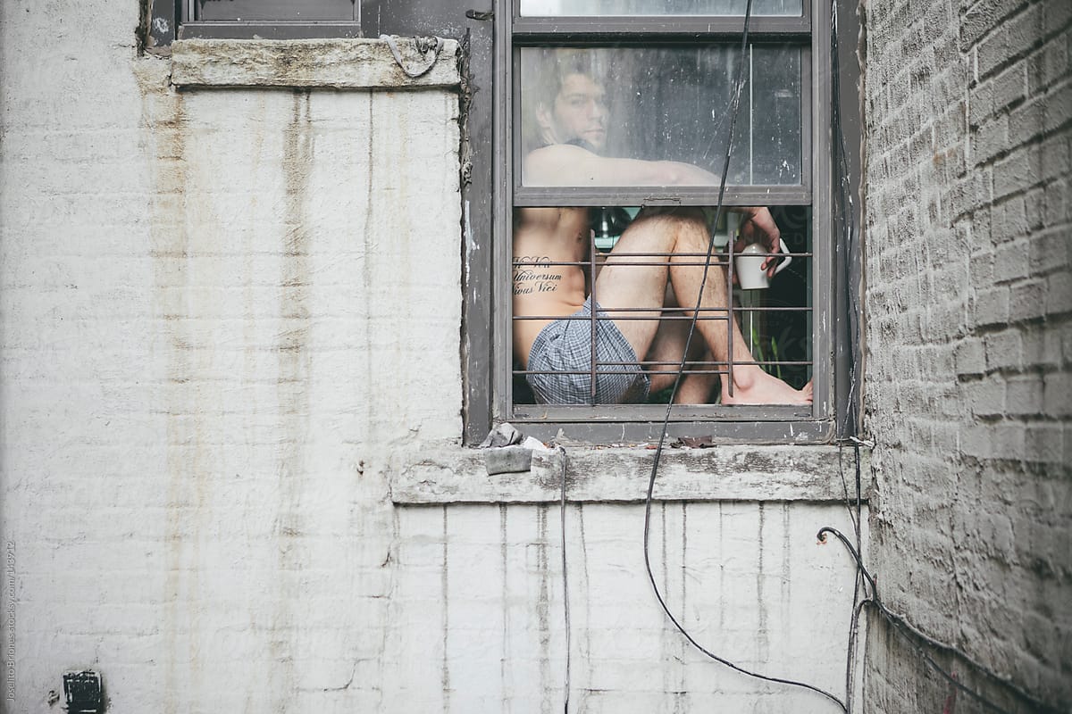 Shirtless Man in Boxer Shorts Drinking Coffee Sitting at Window of Urban Apartment