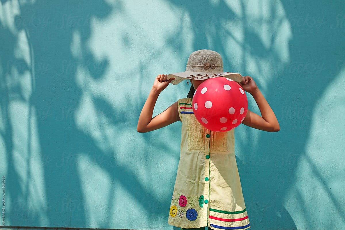 A girl conceal his face with a red balloon with shady background