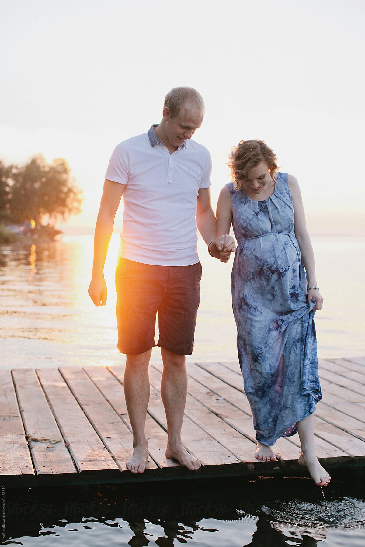 Happy couple standing on a pier on river and pregnant woman touching the water with feet