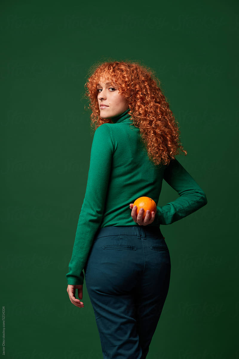 Curly redhead lady with orange behind back