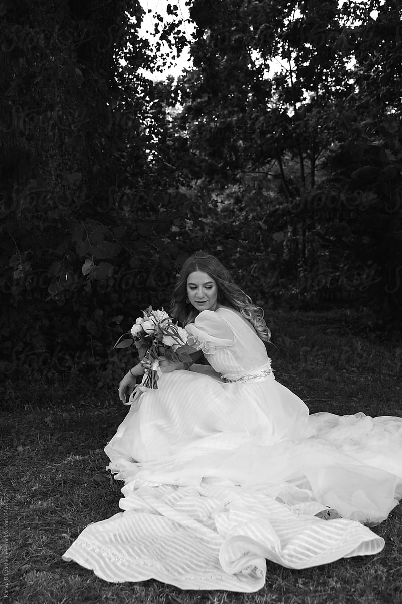 black and white portrait of a bride in an airy dress with a long train sitting in the forest during a wedding walk