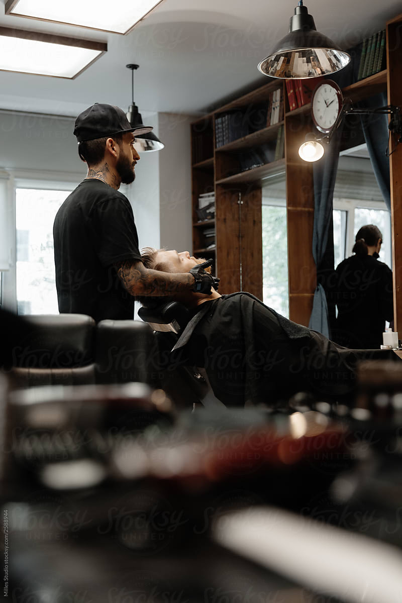 Professional barber grooming young man in salon
