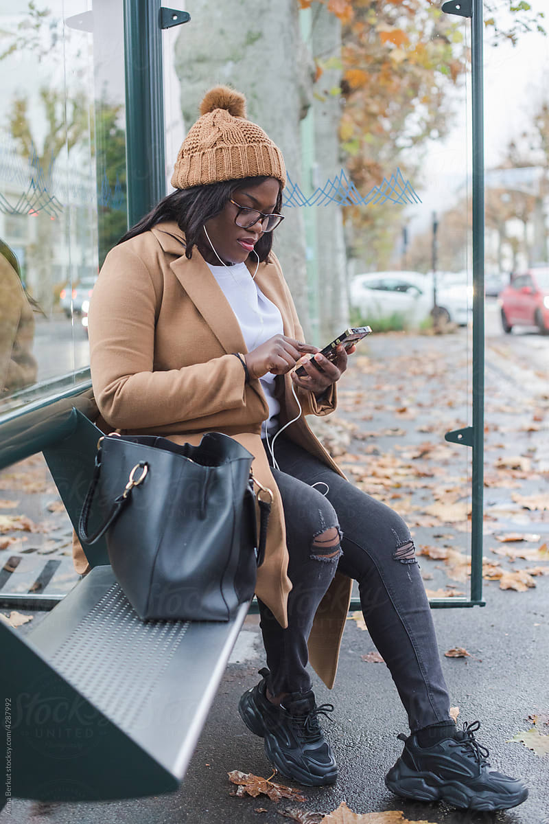 black woman using smartphone on bus stop, transport passenger