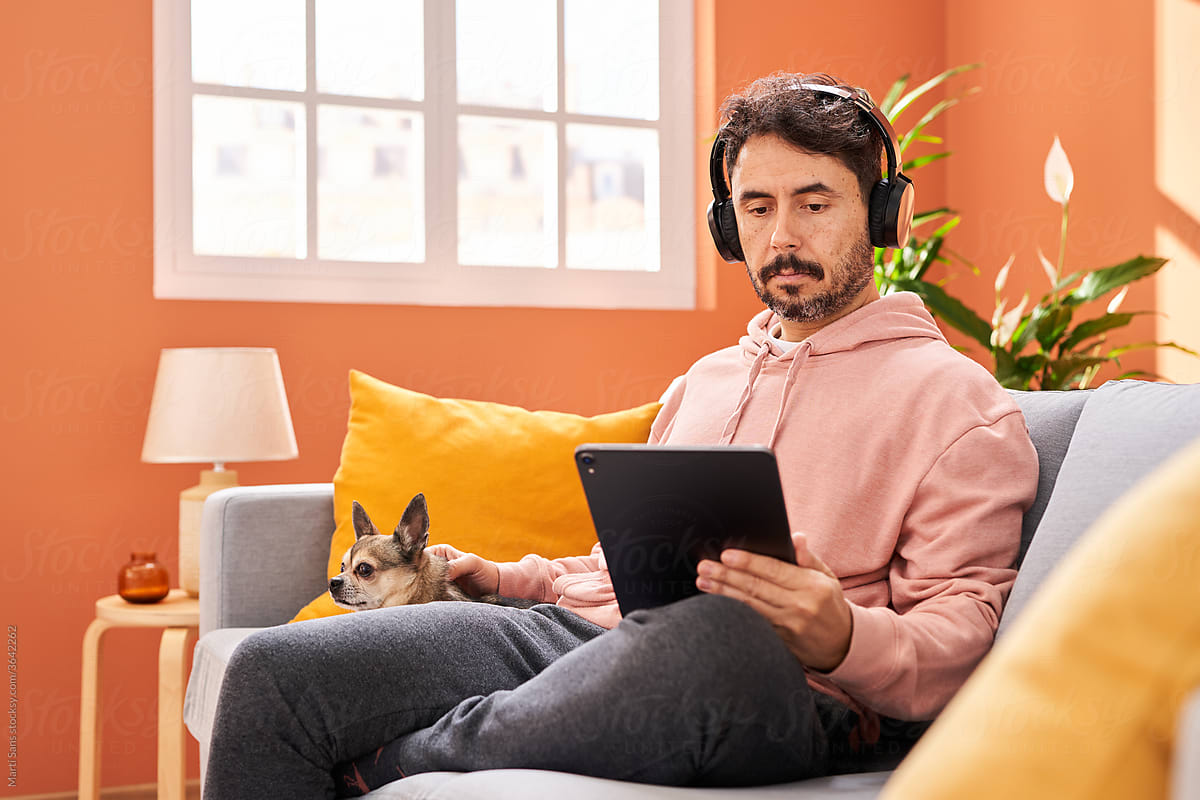 Man petting dog and using tablet on sofa