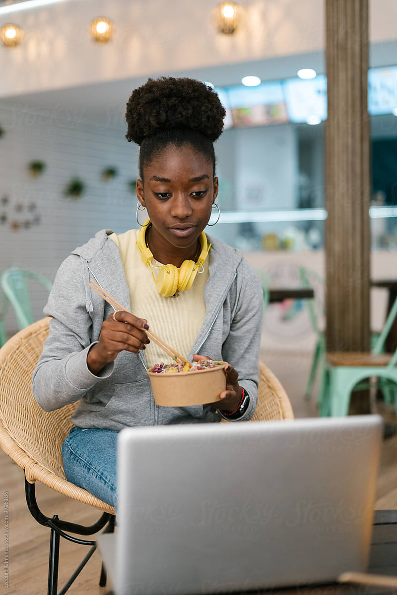 Black woman eating while looking at her computer
