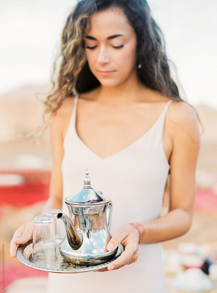 A portrait of a dark-haired woman serving moroccan mint tea in the desert