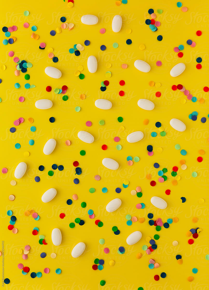 Pills and confetti scattered on a bright yellow background