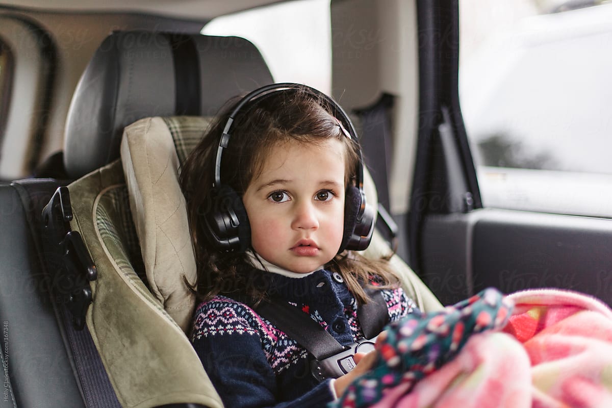 A young child wears headphones in the back of a car.