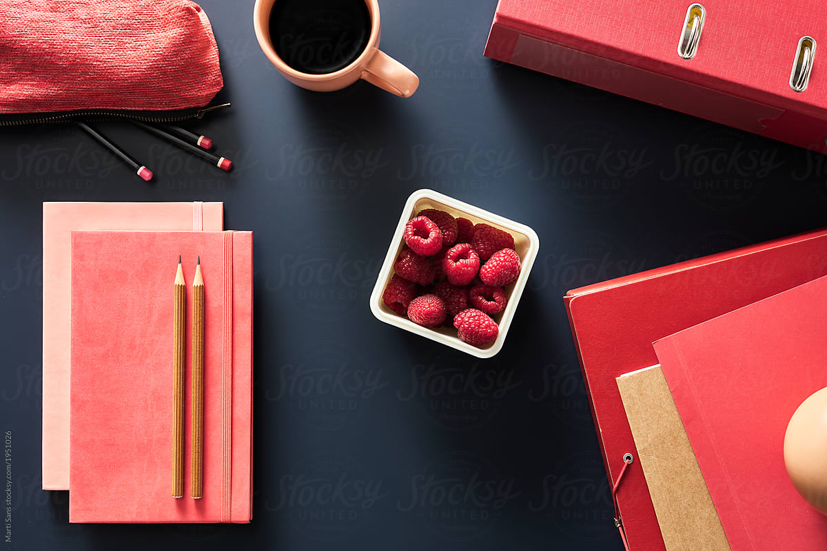 Container of fresh raspberries with notebooks on desk
