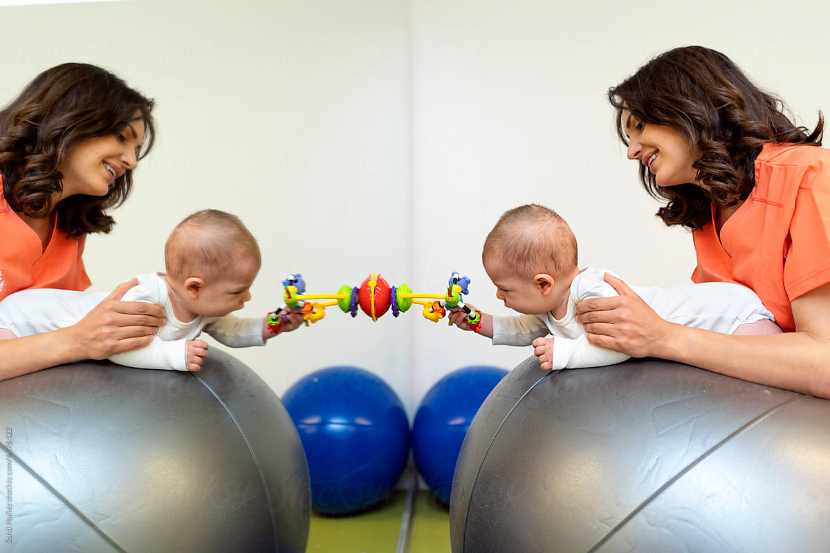 Young nurse exercising baby on fit ball near mirror