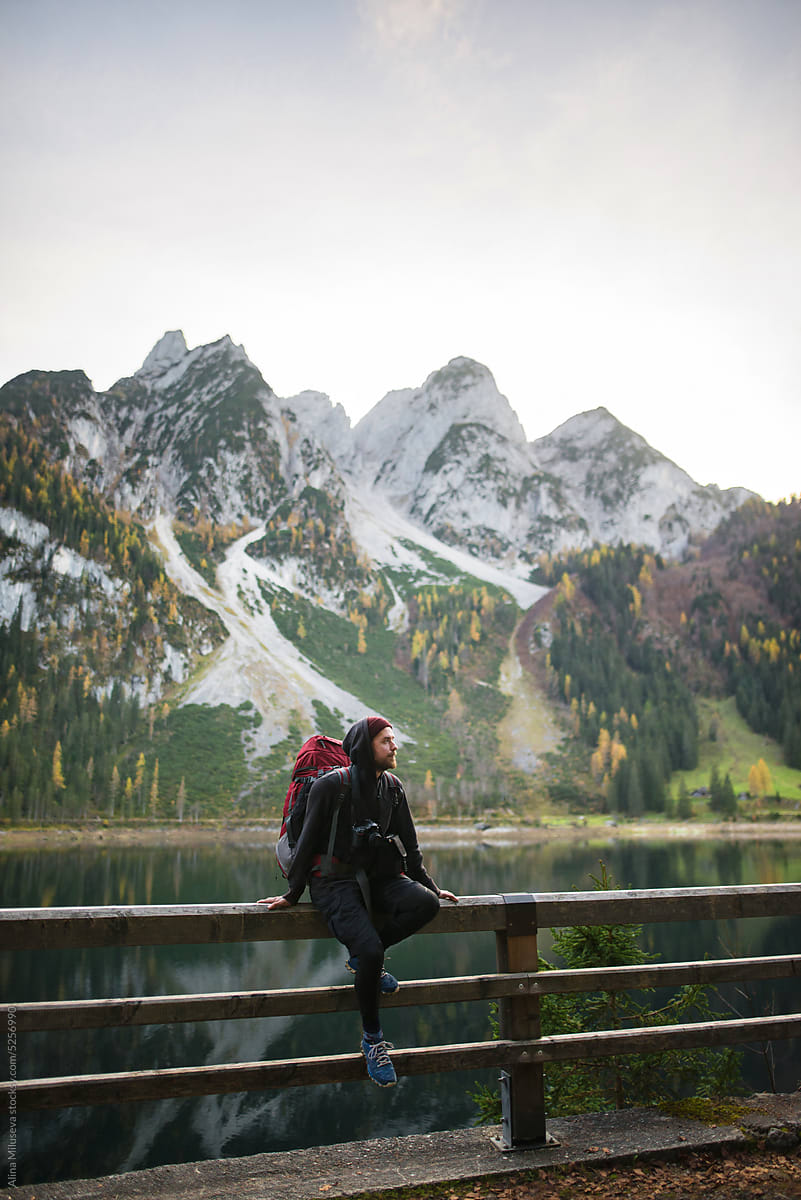 Traveler With Backpack Sitting Near Lake And Mountains