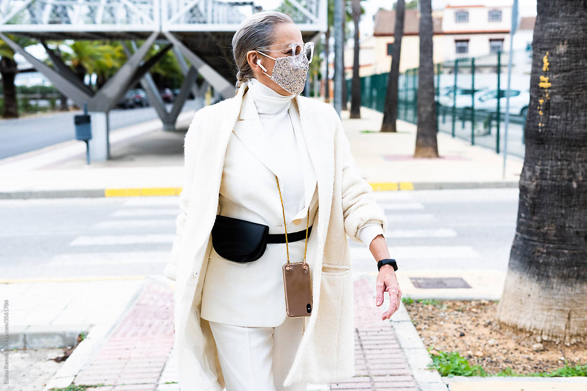 senior business woman walking down street wearing mask and headphones