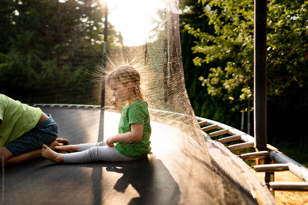 Girl with staticky hair sits on trampoline in strong light