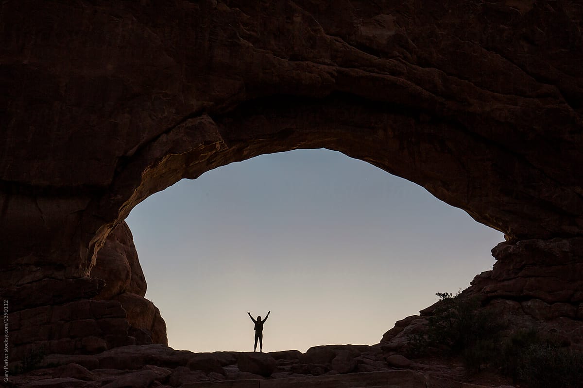 A woman stretching beneath a rock arch cave on sunrise
