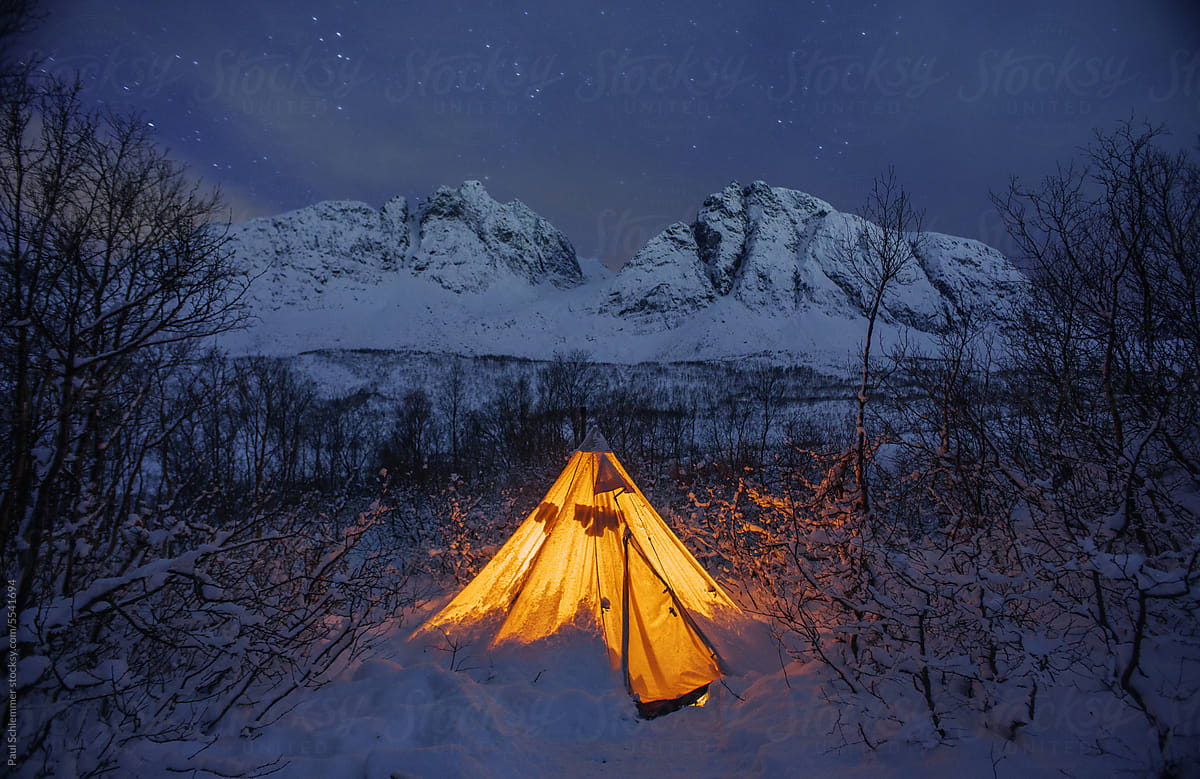 Winter camping, glowing canvas tent at night,snow mountains background