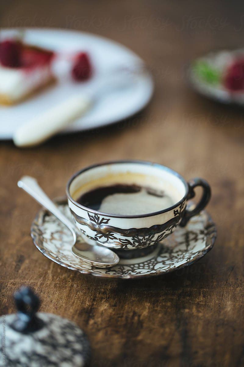 Black espresso coffee cup served in vintage decorated china cup with fruit cake on background