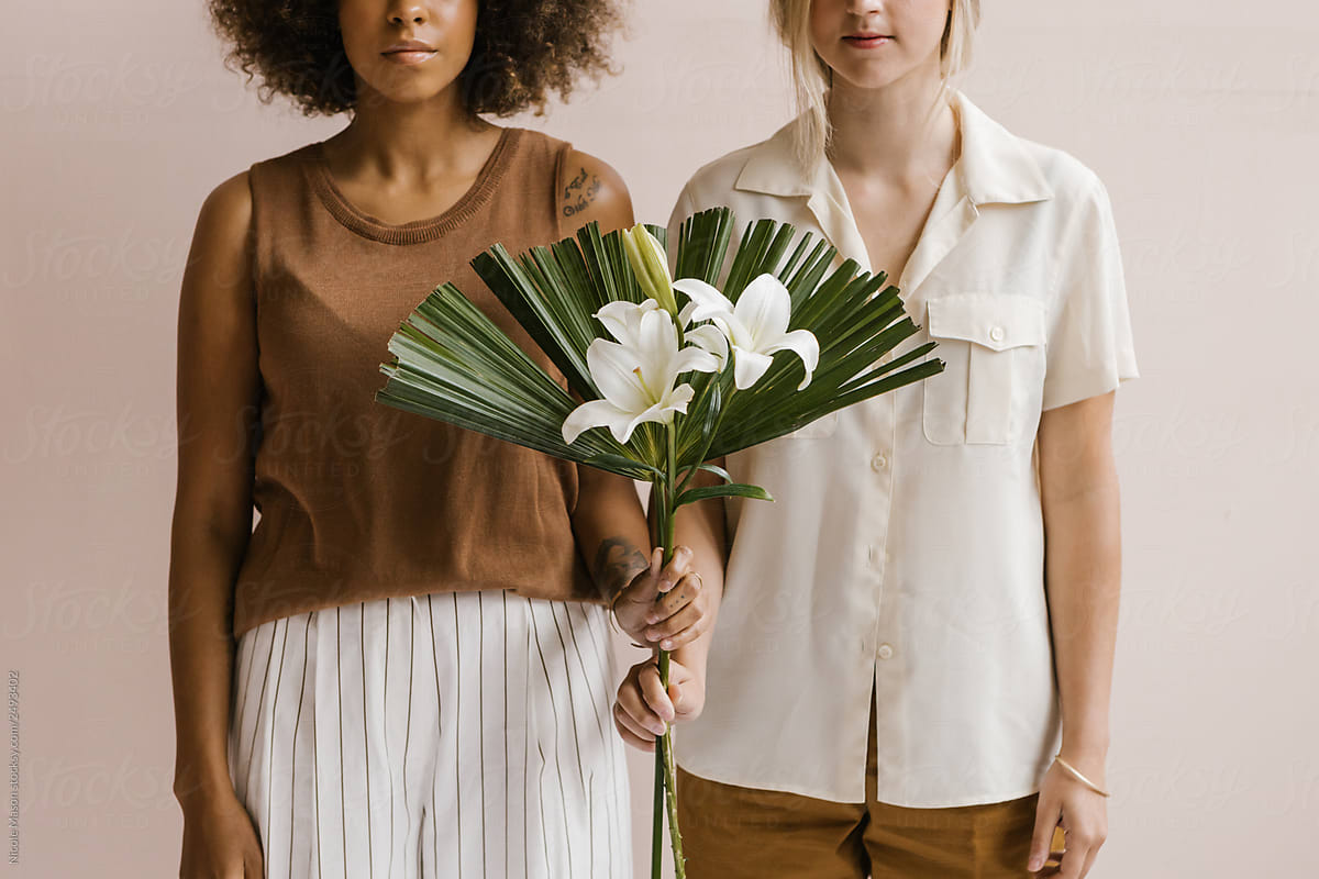 two young stylish women posing together holding florals and tropical leaves