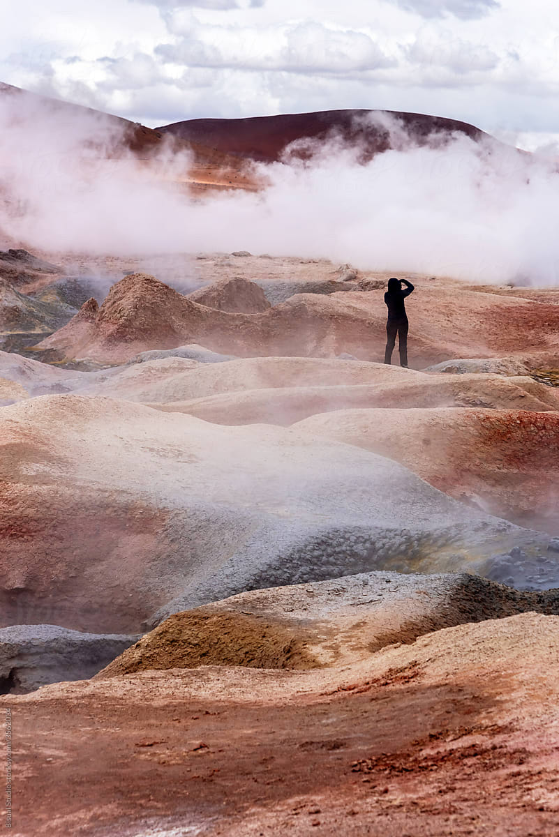 Woman taking a photo of some geysers with volcanic activity and mud pits