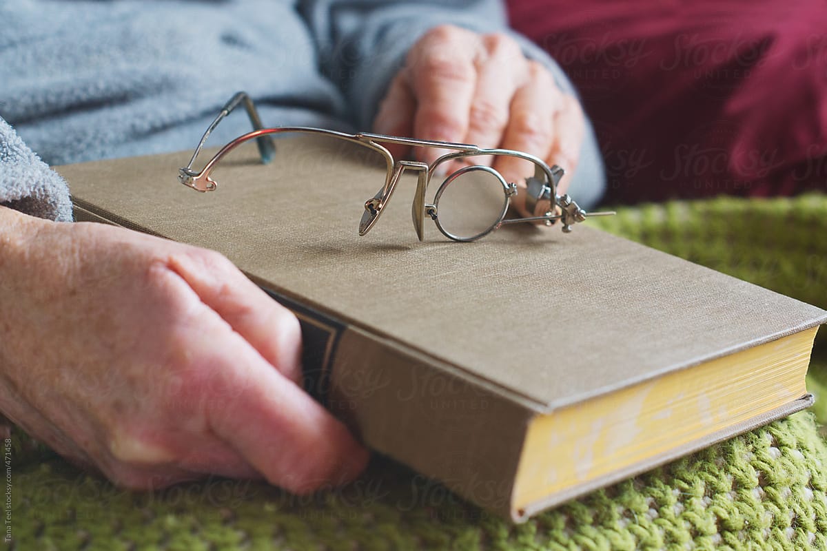 Homemade reading glasses placed on a book held by older woman
