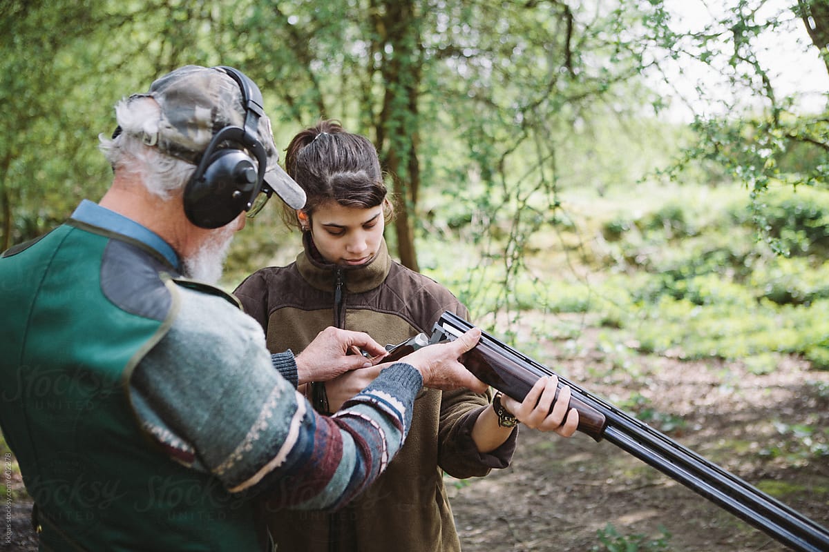 Young girl learning to fire a shoot gun in a firing range with an instructor .