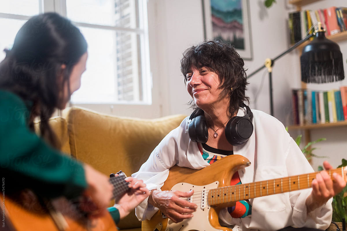Smiling mother enjoying guitar playing with adult daughter