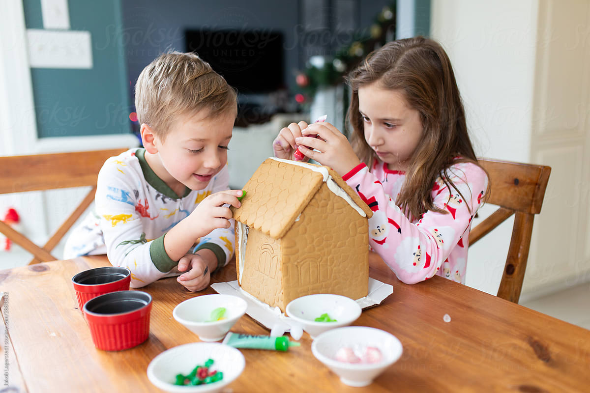 Brother and sister decorating a gingerbread house for the holidays