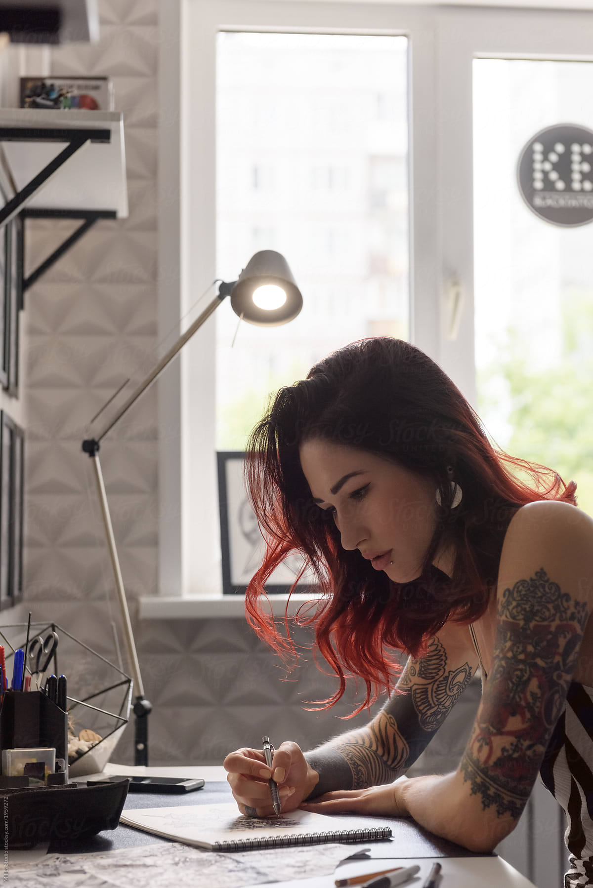 Young tattooed girl drawing at desk
