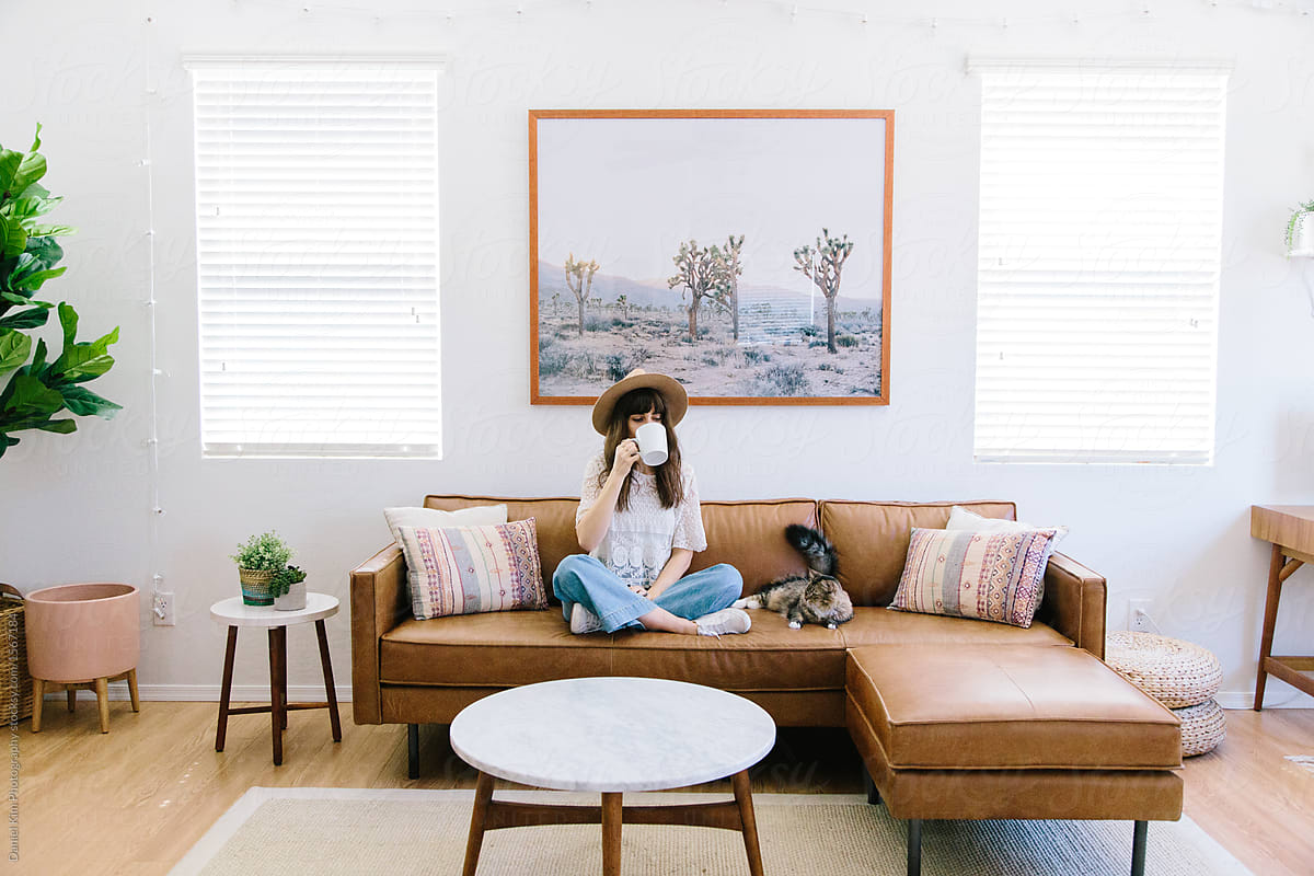 Woman Sitting On Couch In Living Room Drinking Coffee Next To Cat by Daniel  Kim Photography