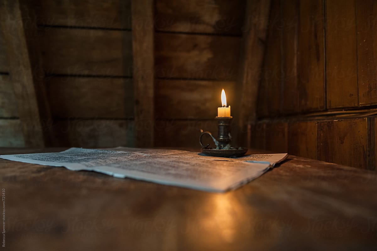 Candle light illuminates a newspaper on table