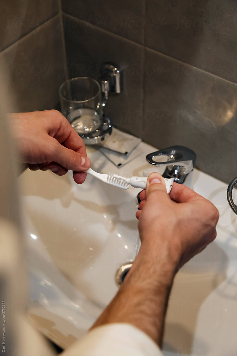 Crop faceless man putting toothpaste on brush in bathroom